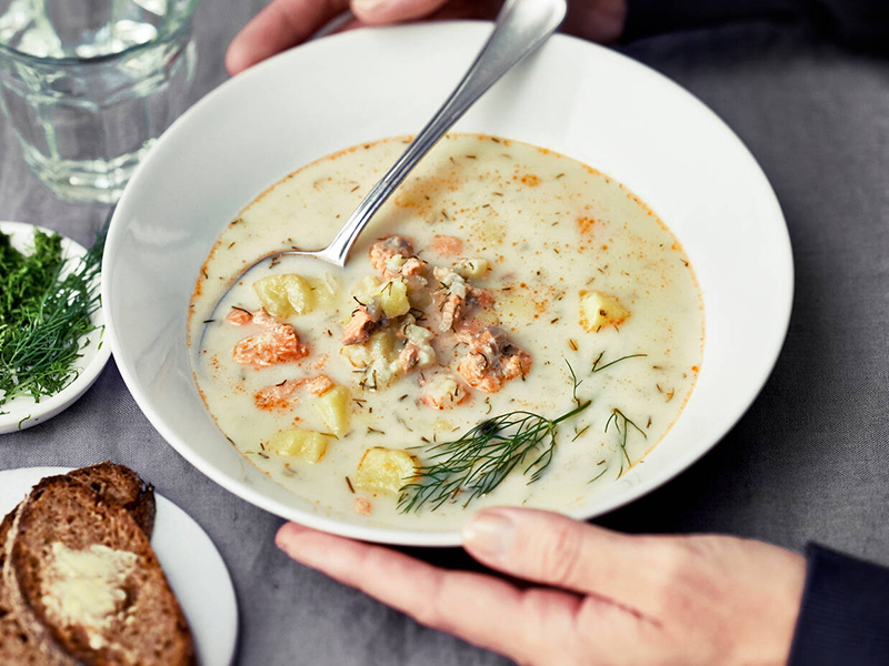 Kuvassa on lautasella kirjolohikeittoa, pöydällä ruisleipää ja vesilasi.