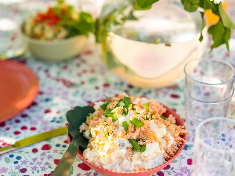 Kuvassa on kesäinen pöytä ulkona ja kulhossa raastesalaattia