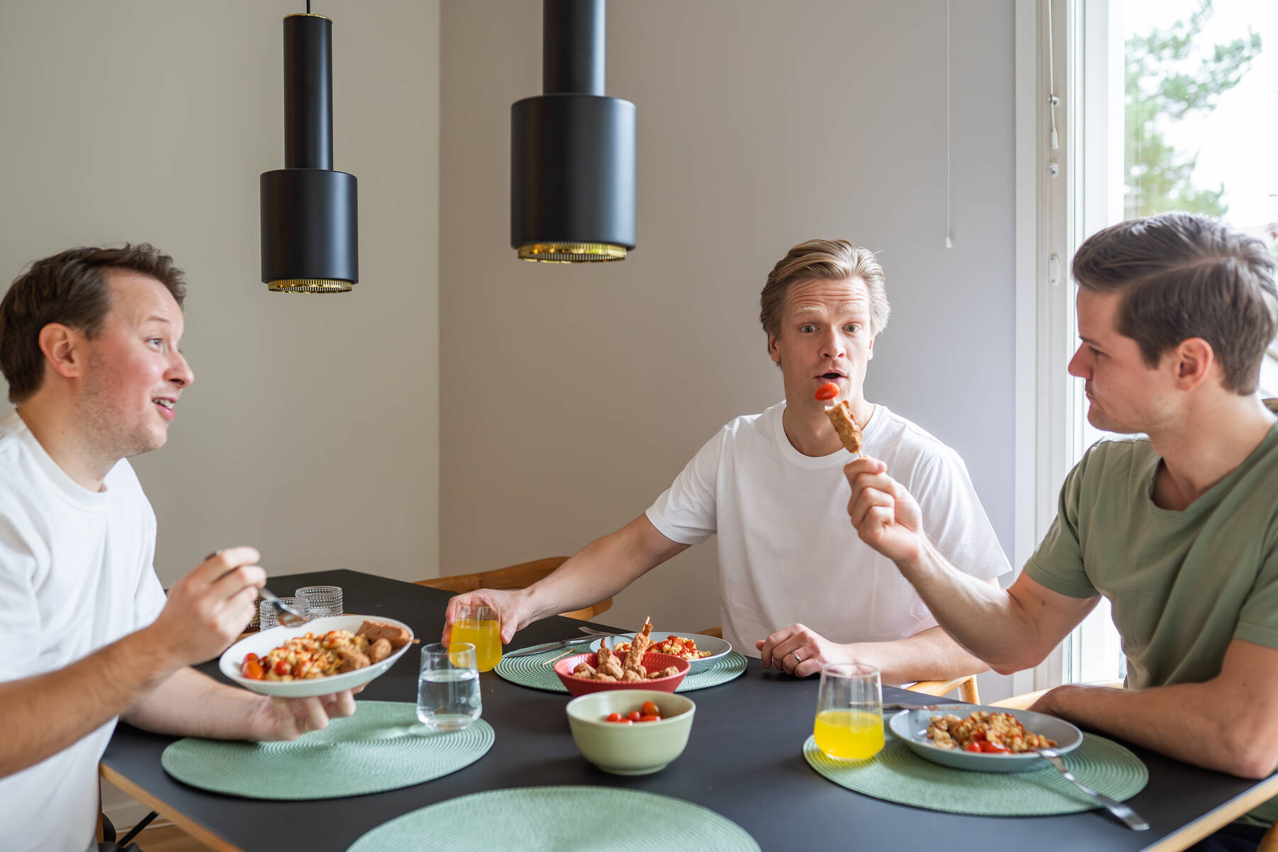 Kuvassa on kolme henkilöä ruokapöydän ääressä syömässä yhdessä.