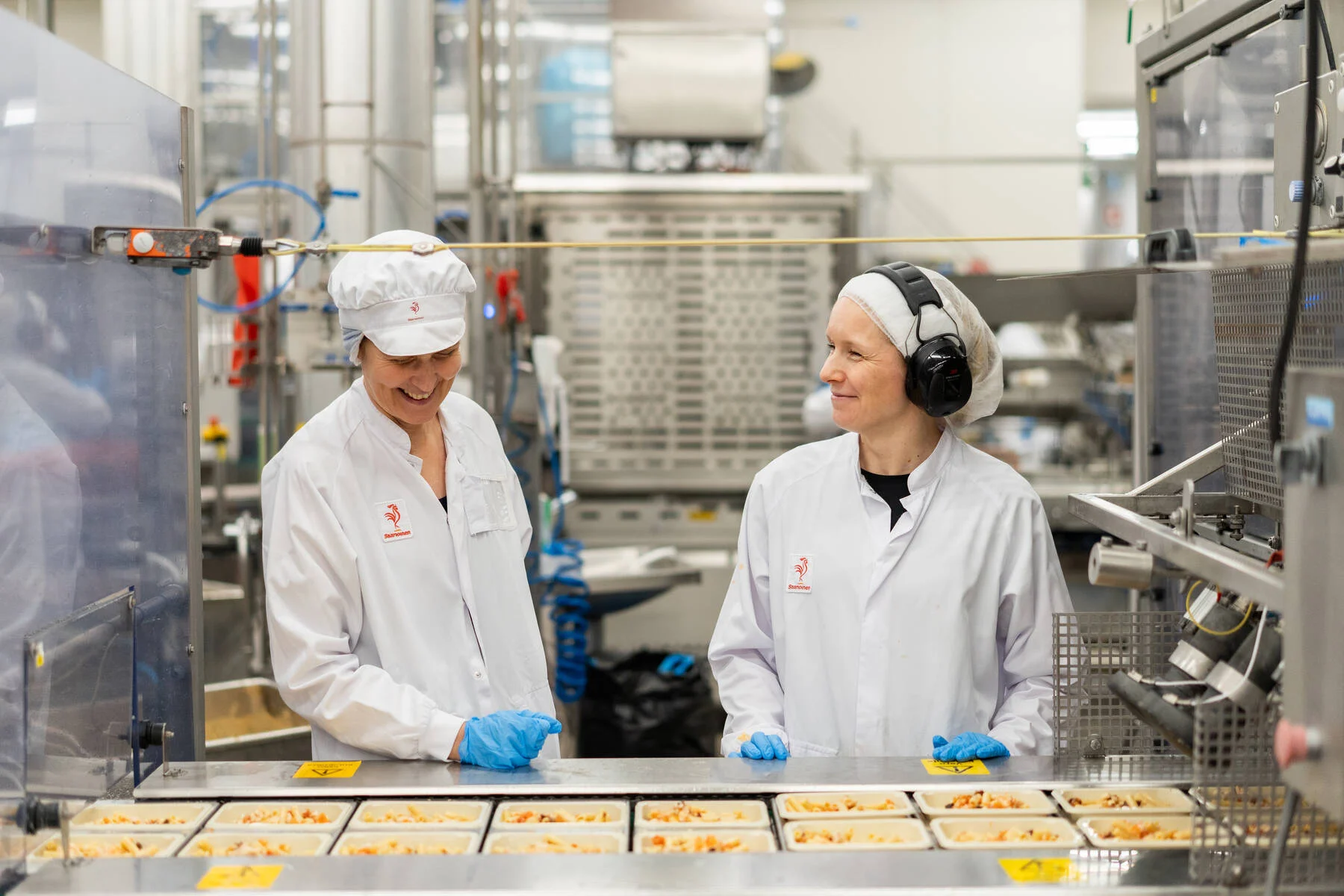 Kuvassa on kaksi henkilöä vieritysten katsomassa tehdaslinjaa.