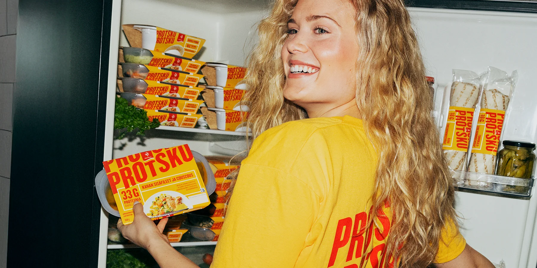 Kuvassa on henkilö jääkaapilla hakemassa protsku-tuotteita ja t-paidan selässä lukee 3 x protsku