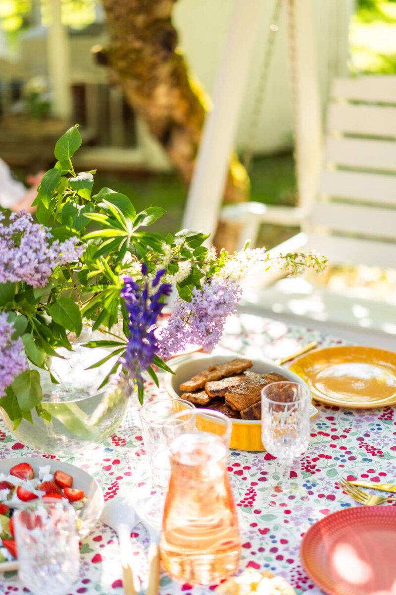 Kuvassa on kesäinen ruokapöytä puutarhassa ja pöydässä astioita ja grilliruokaa
