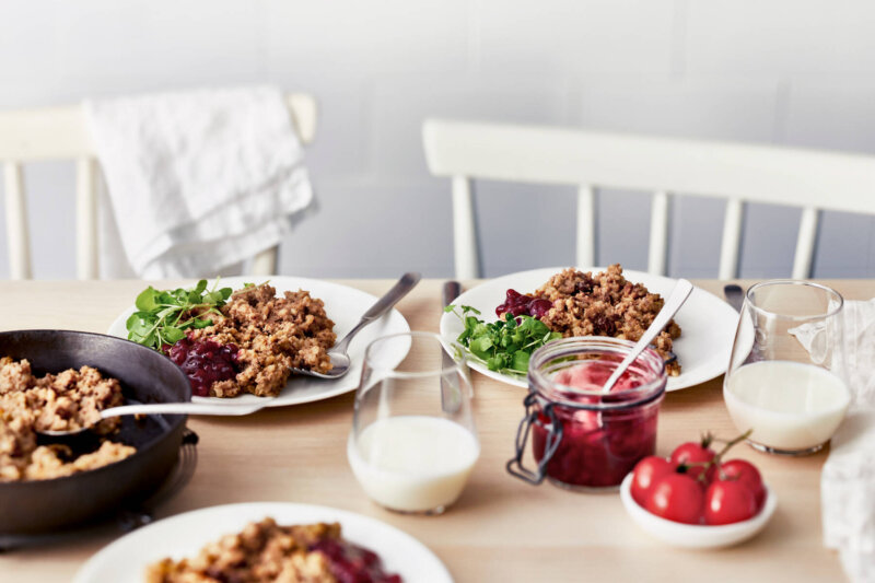 Ruokapöydässä lautasia, joissa maksalaatikkoa ja puolukkahilloa