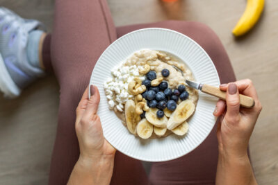 Lattialla istuvan urheilijan sylissä puurokulho ja lattialla banaani.